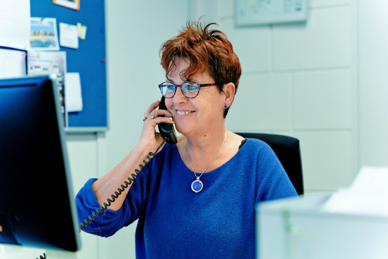 Vrouw in blauw aan de telefoon achter computer