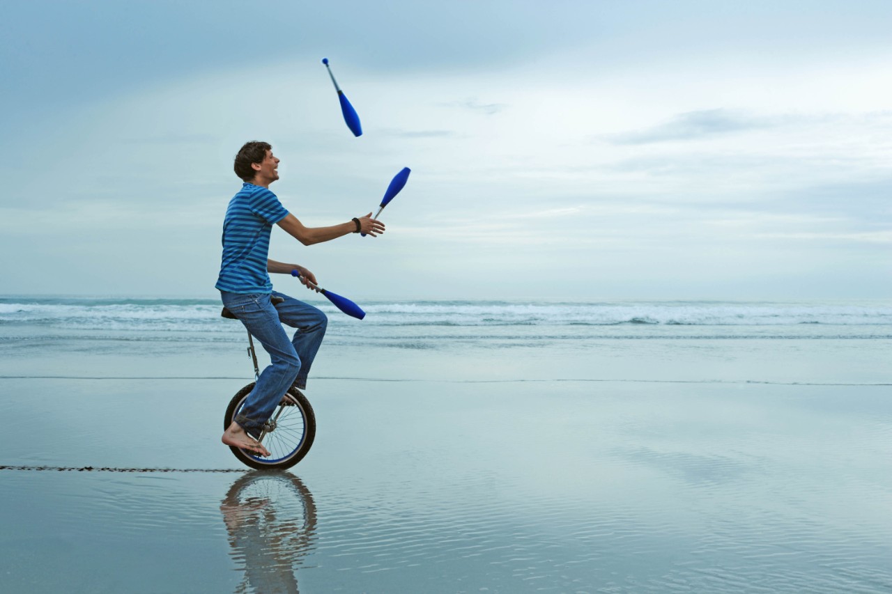 man op eenwielier jongleert op het strand