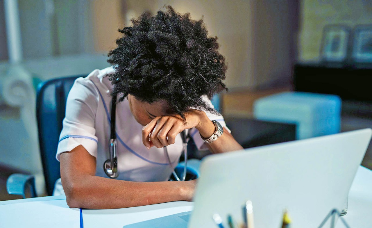 Dokter achter laptop met hoofd tegen hand