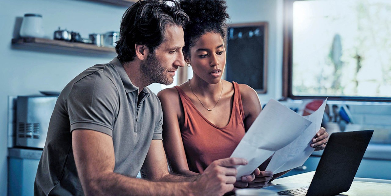 Man en vrouw kijken naar papier en zitten voor laptop