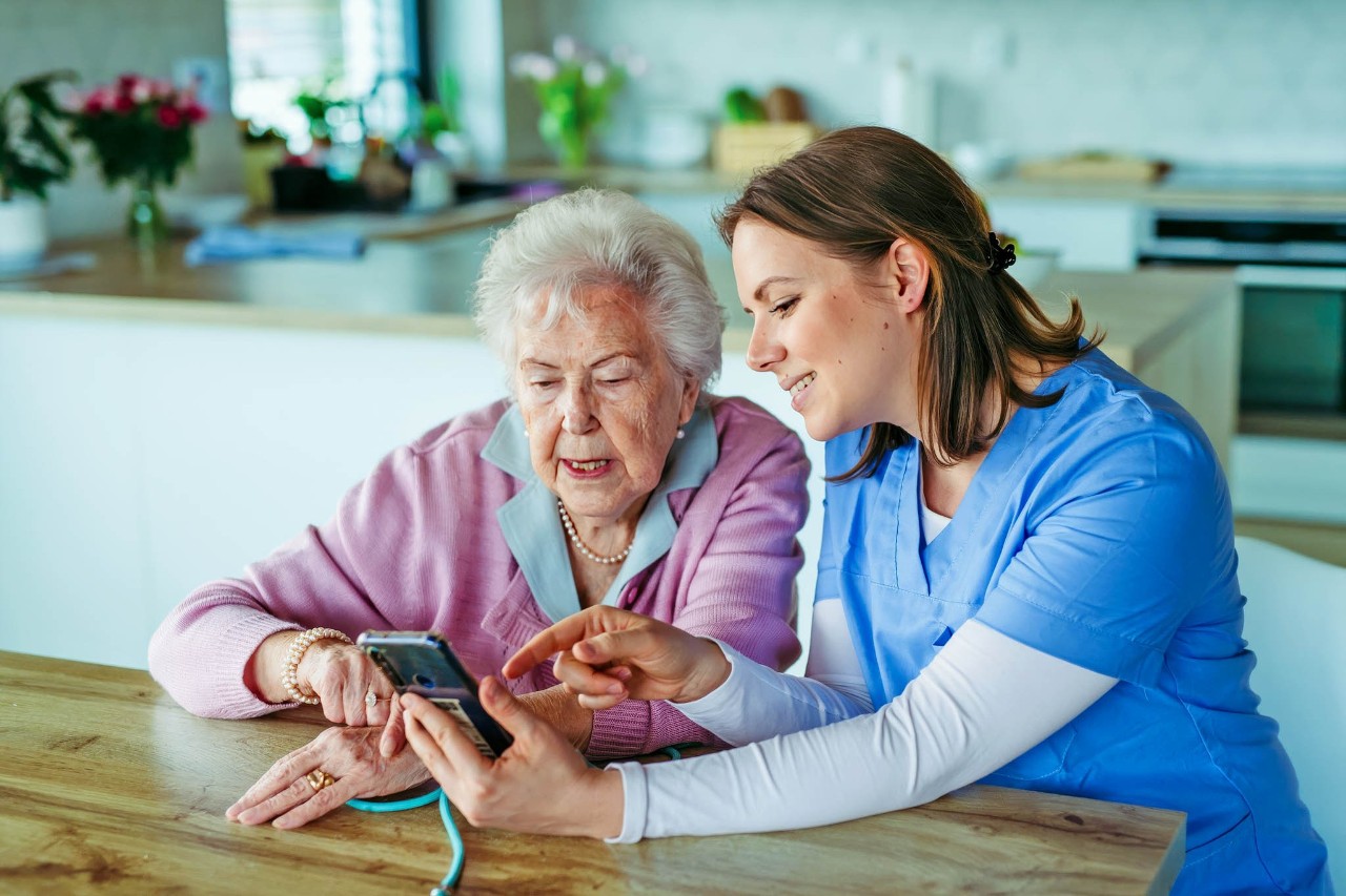 Verzorger kijkt mee met oudere dame op telefoon