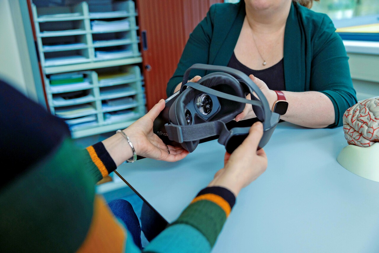 Patiënt heeft VR-bril vast en zit aan tafel met Kyra