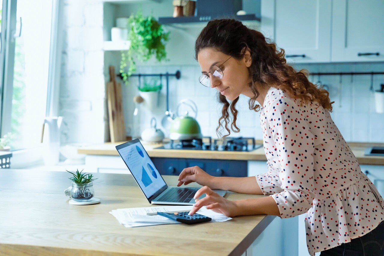 Vrouw met laptop en rekenmachine in keuken 