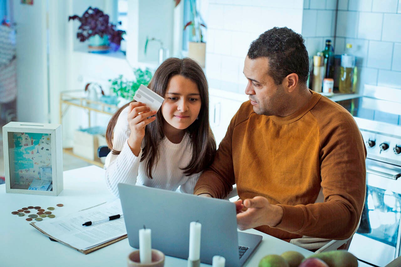 Vader en dochter met laptop pasje en geld aan tafel