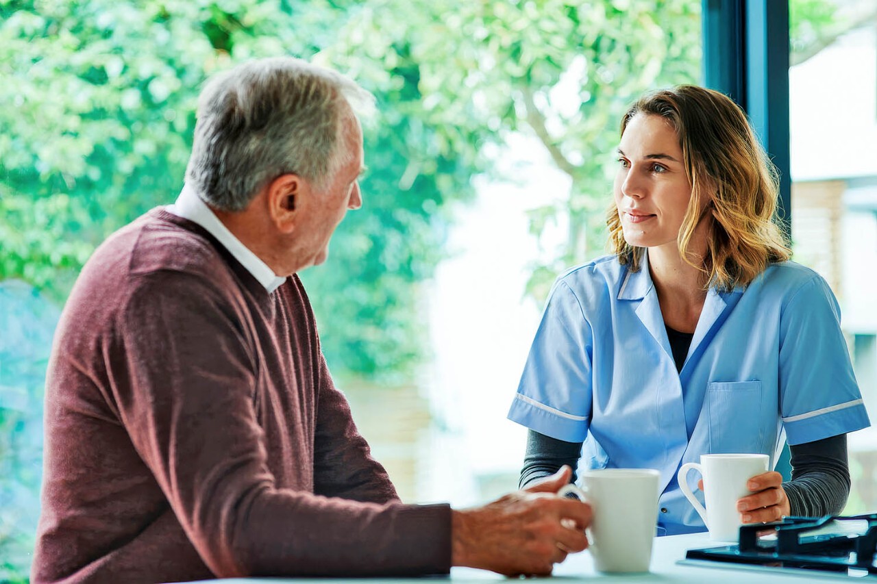 Zorgmedewerker en man drinken koffie aan tafel