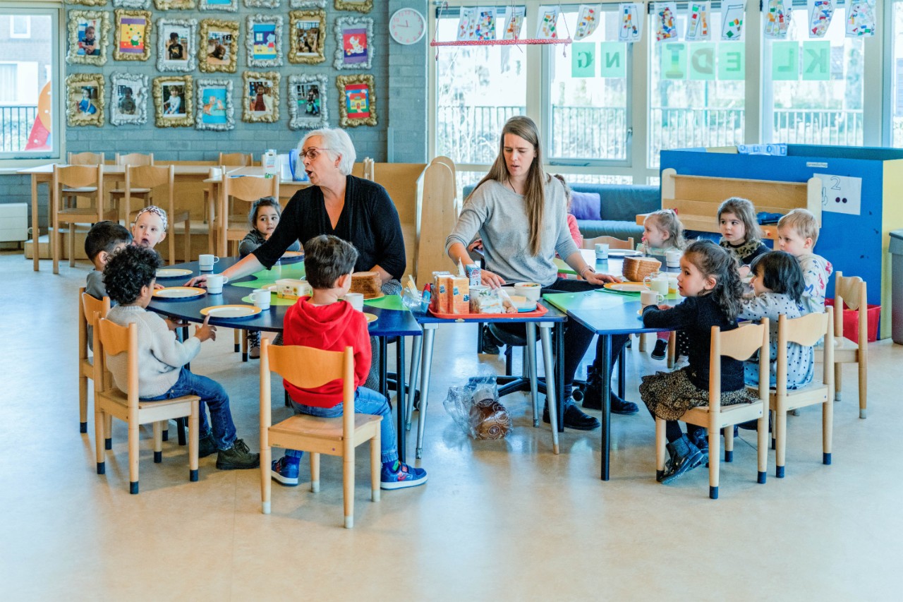 Kinderen tijdens lunch aan tafel met kinderjuffen